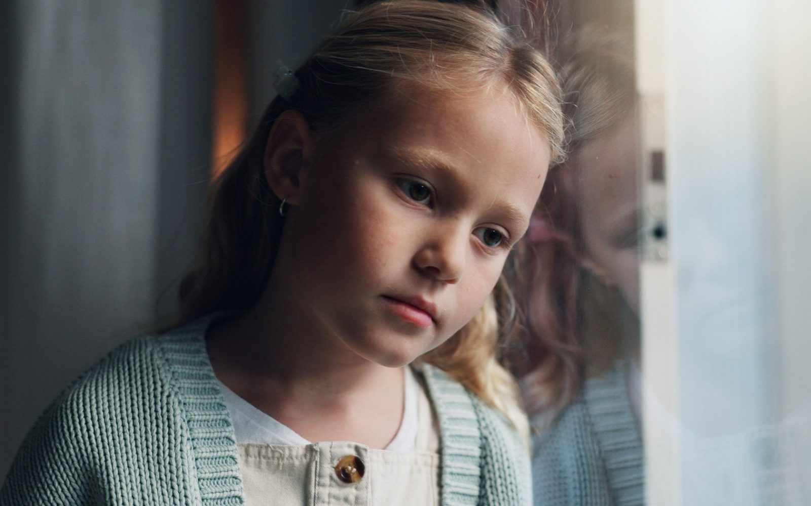 Žalostna, zapuščena, travmirana in razmišljajoča deklica strmi v okno