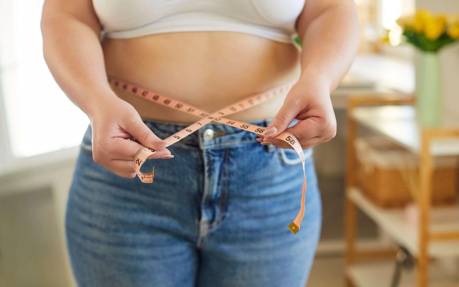 Ženska meri obseg trebuha z merilnim trakom – hujšanje ne napreduje zaradi prenizkega vnosa kalorij.