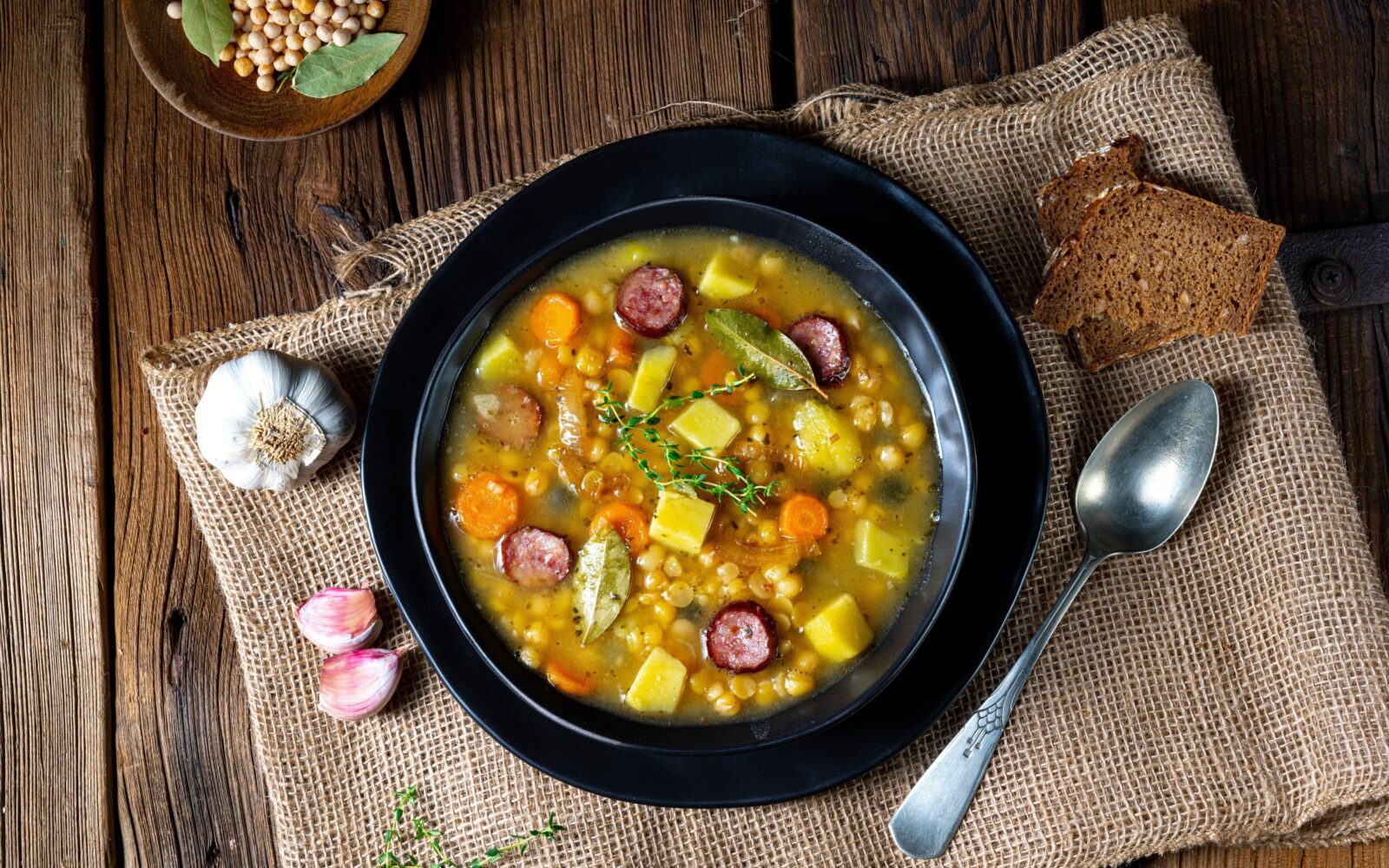 Juha s fižolom, grahom, klobaso, krompirjem, korenjem in česnom v krožniku na pogrinjku - okusen jesenski obrok