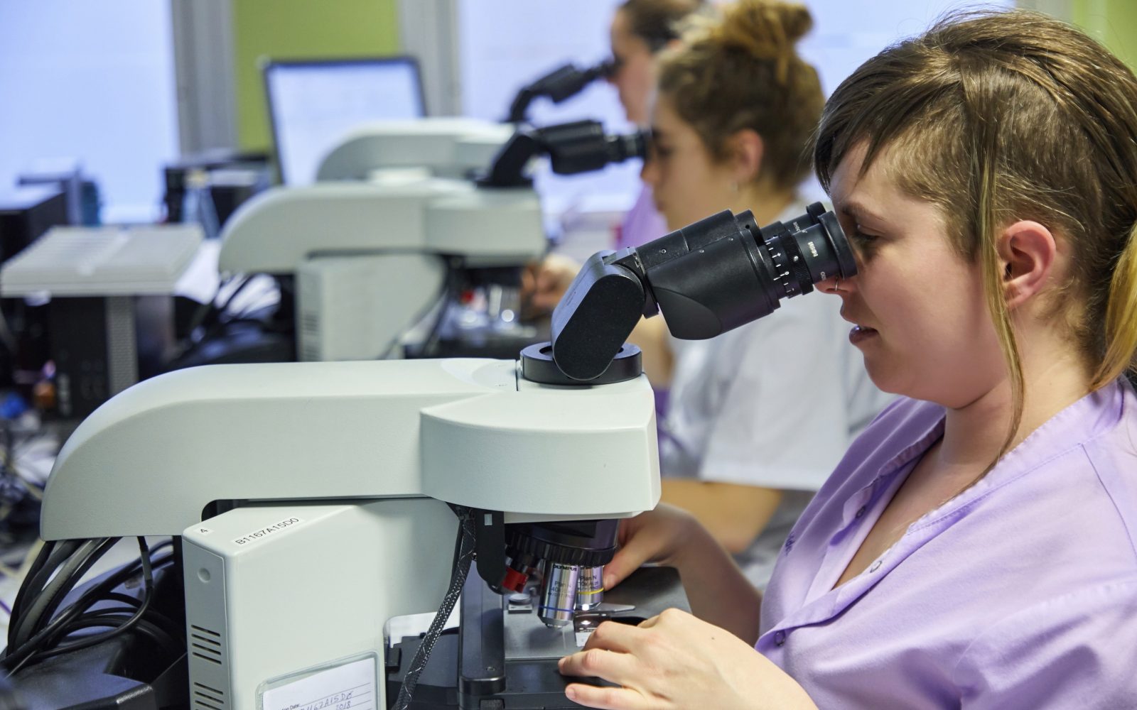 Zdravstvena delavka pod mikroskopom pregleduje vzorce v laboratoriju – simbol prizadevanj Koroške za preprečevanje raka materničnega vratu.