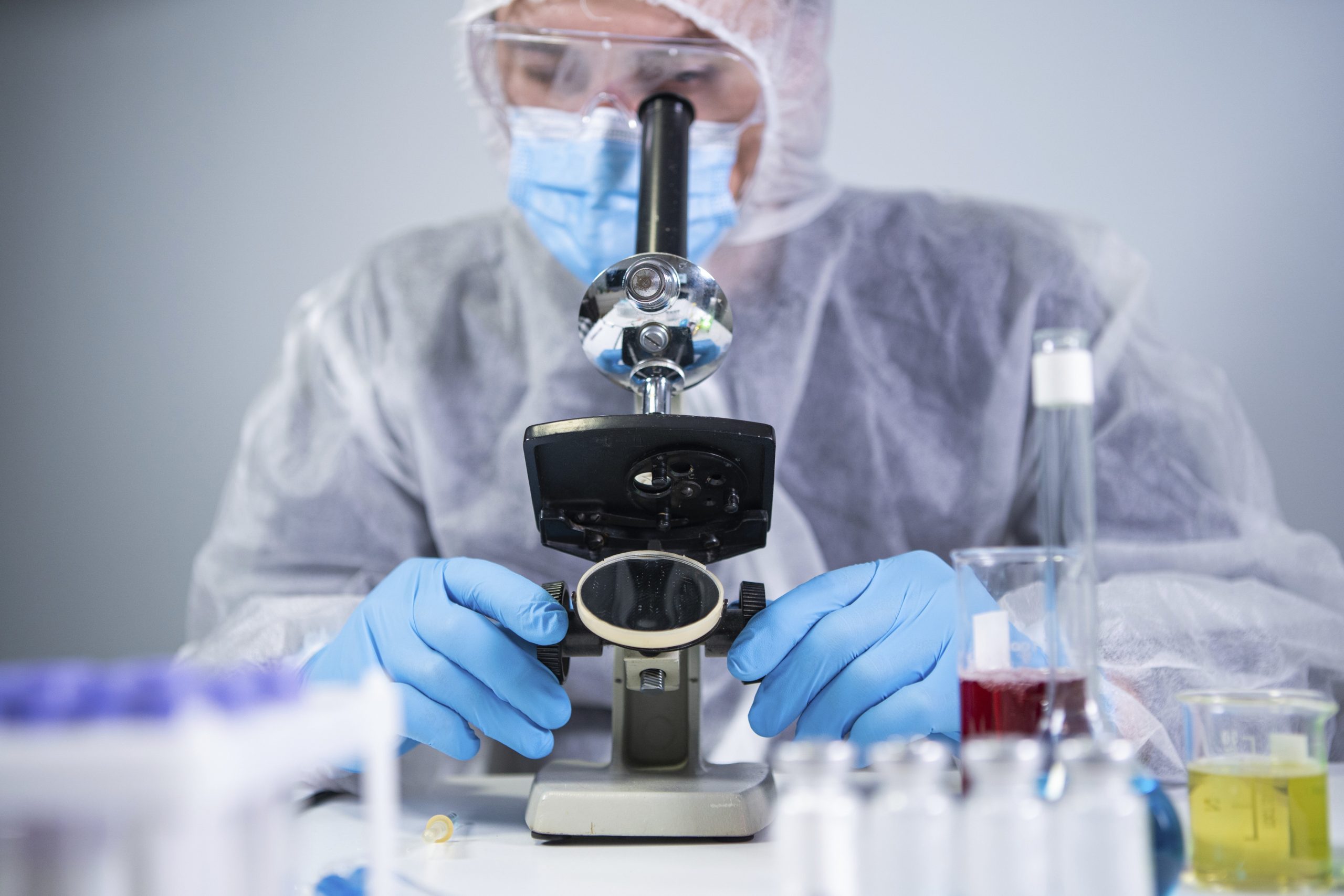 Znanstvenik v laboratoriju pod mikroskopom analizira prisotnost kemikalij PFAS, povezanih z vplivom na zdravje in oblačila.