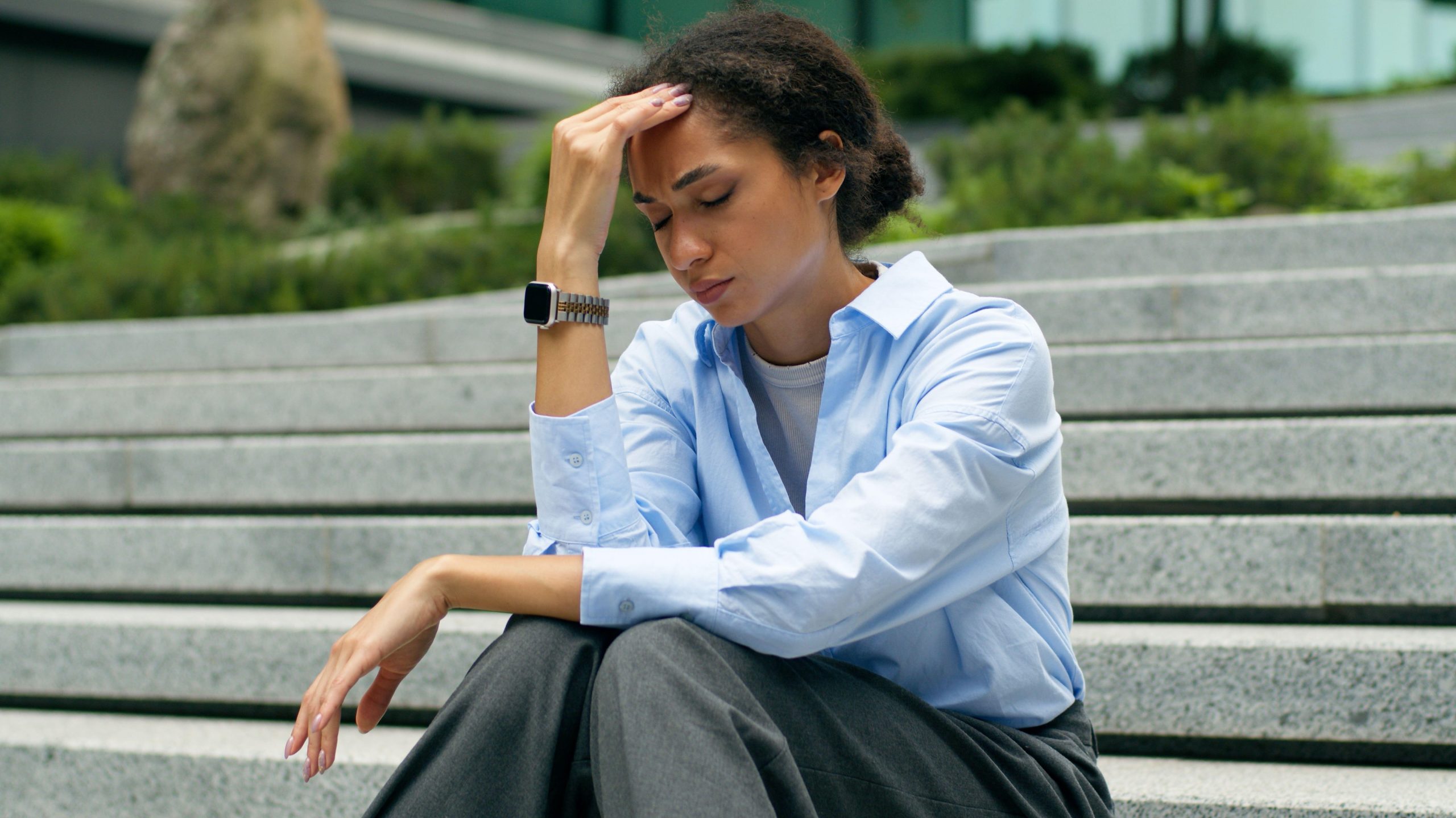 Anksiozna poslovna ženska sedi na stopnicah in se zaradi glavobola zaradi stresa drži za glavo.