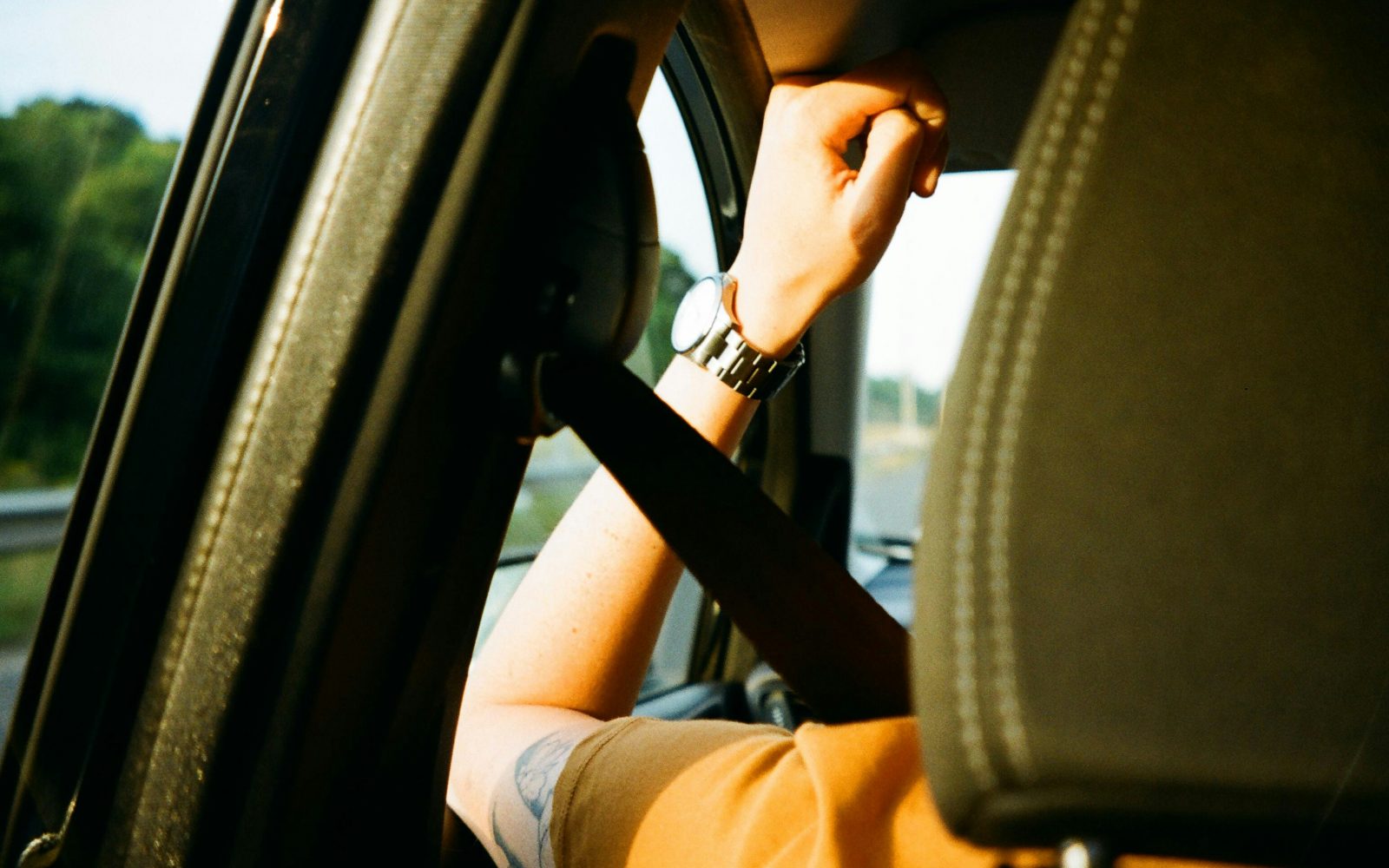 Moški se vozi v avtu, roko ima naslonjeno na odprto okno