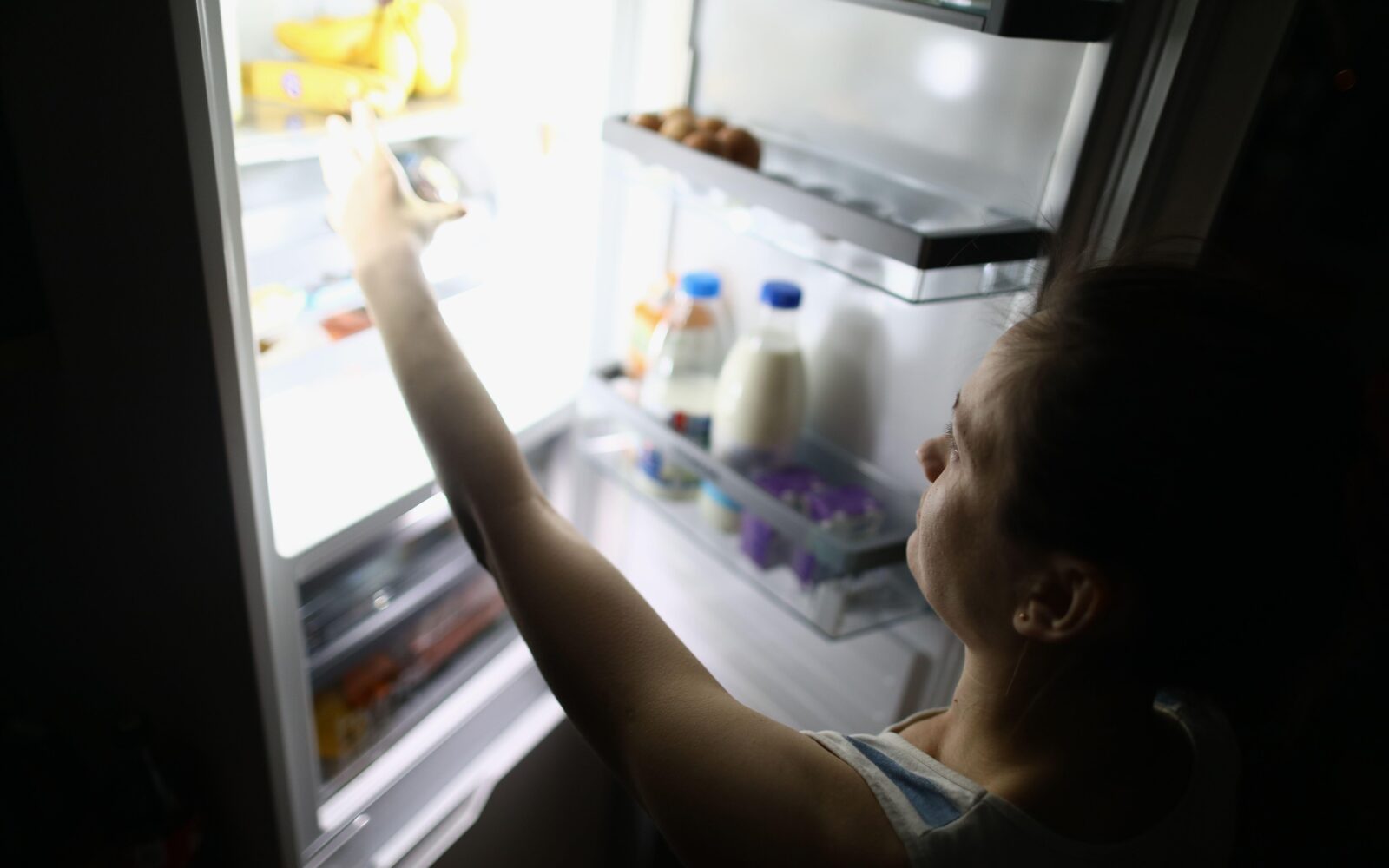 Slika ženske z vrha, kako ponoči jemlje hrano iz hladilnika - posledica ekstremnih diet s spleta