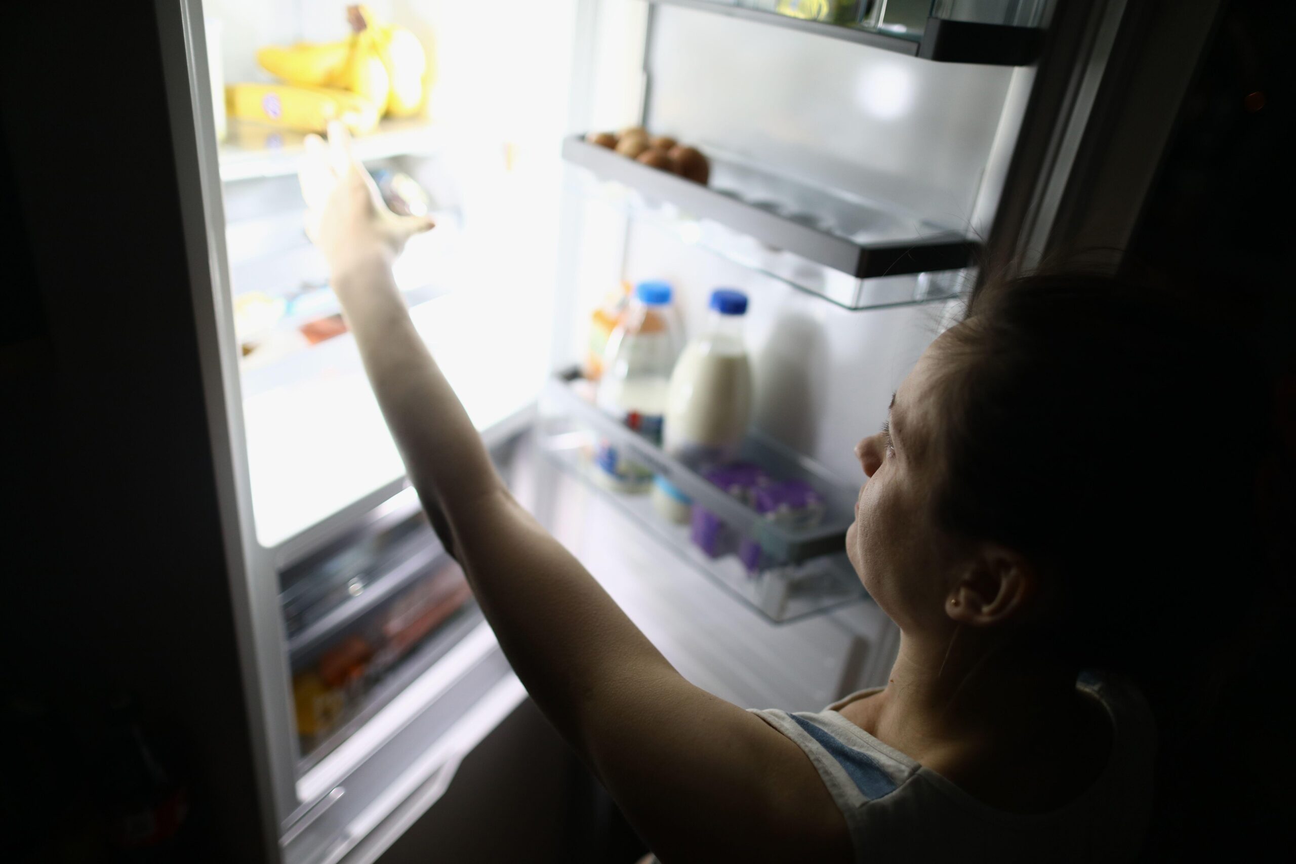 Slika ženske z vrha, kako ponoči jemlje hrano iz hladilnika - posledica ekstremnih diet s spleta