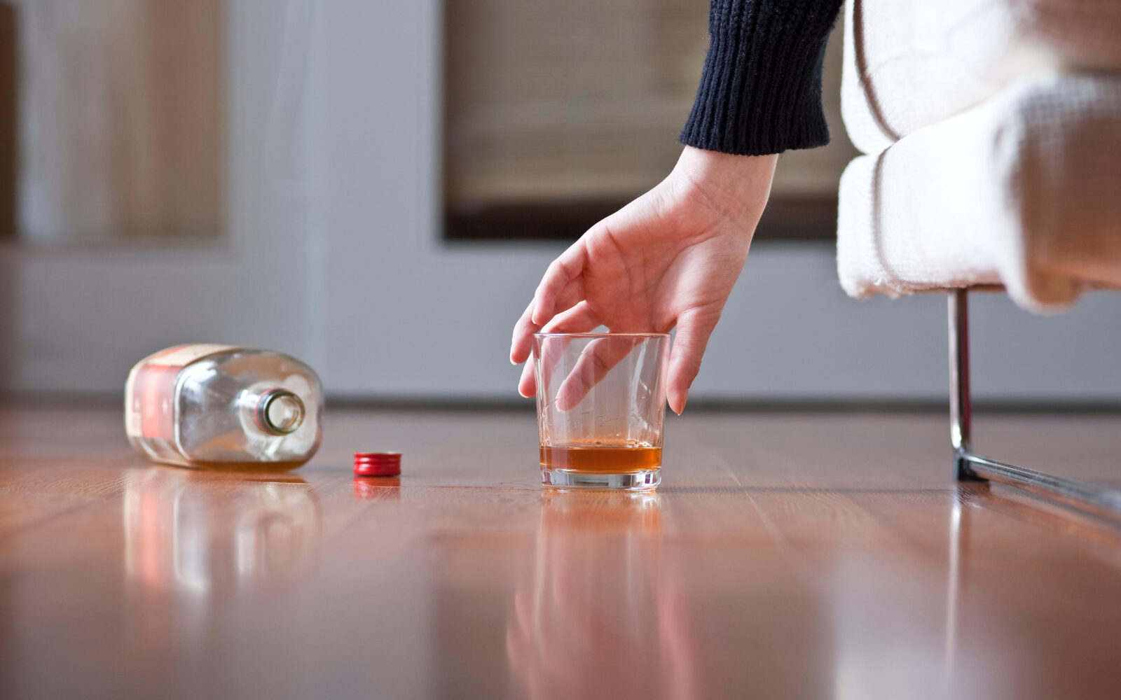 Oseba leži na kavču in z roko sega po kozarcu alkoholne pijače - škodljivi vplivi alkohola na naše telo