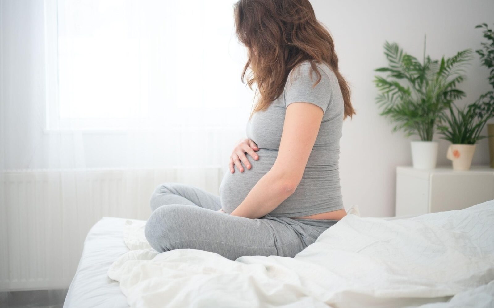 Nosečnica sedi na postelji in se drži za trebuh