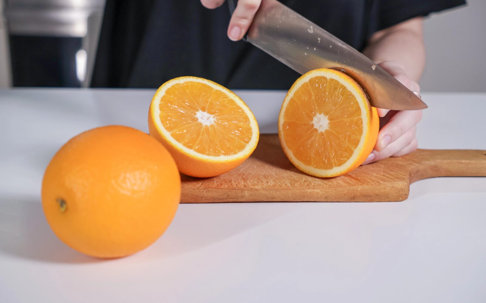 Ženske roke, ki režejo pomarančo na rezalni deski