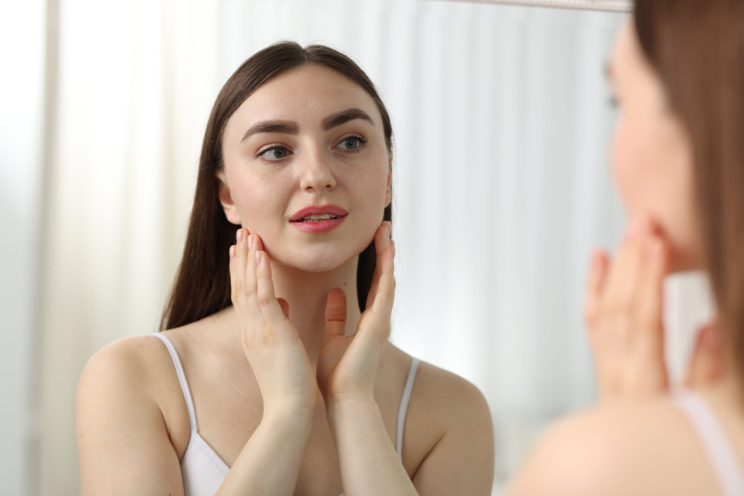 Ženska s sijočo kožo se gleda v ogledalo - posledica izogibanja alkoholu