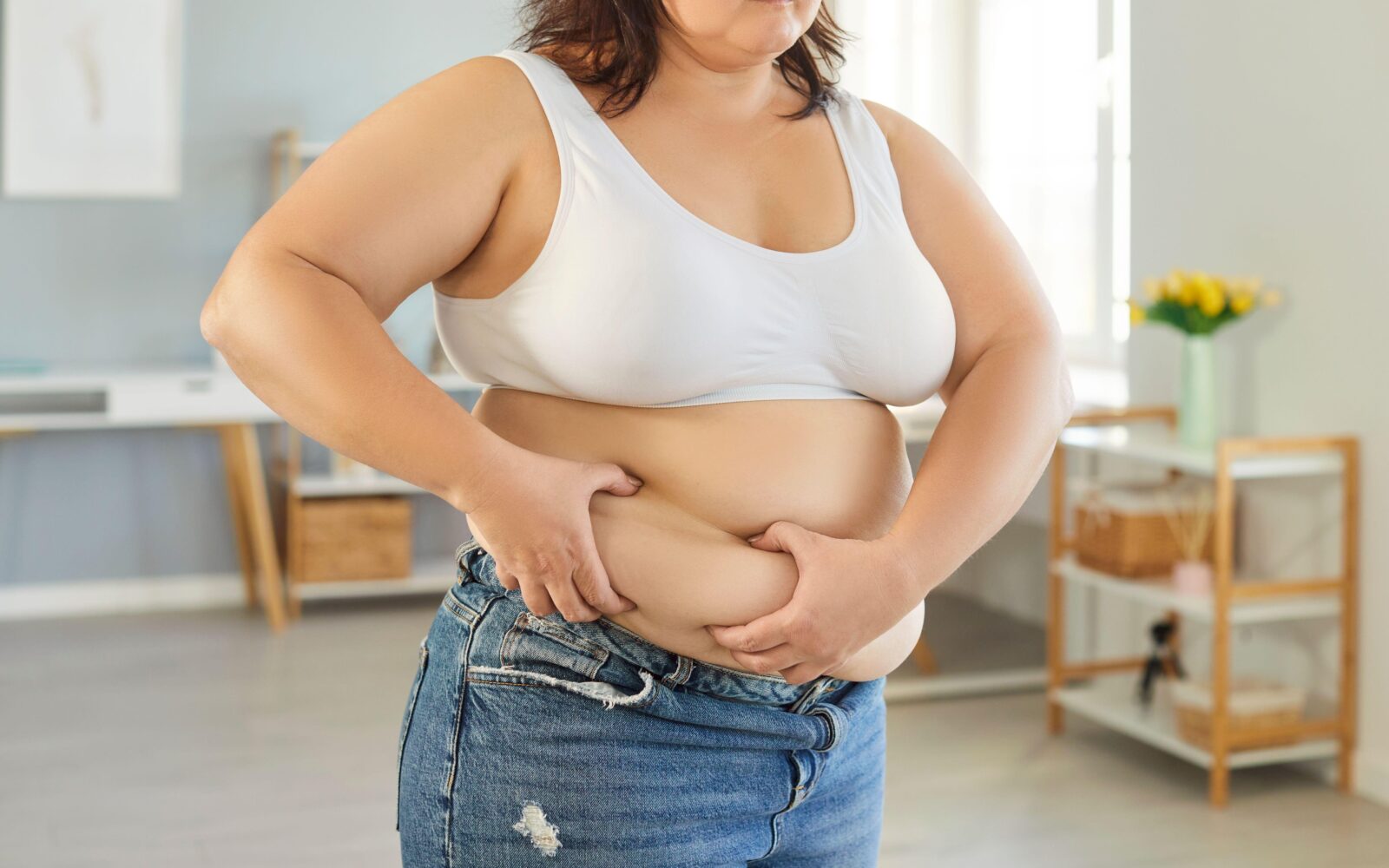 Ženska s prekomerno telesno težo se drži za maščobno tkivo na trebuhu