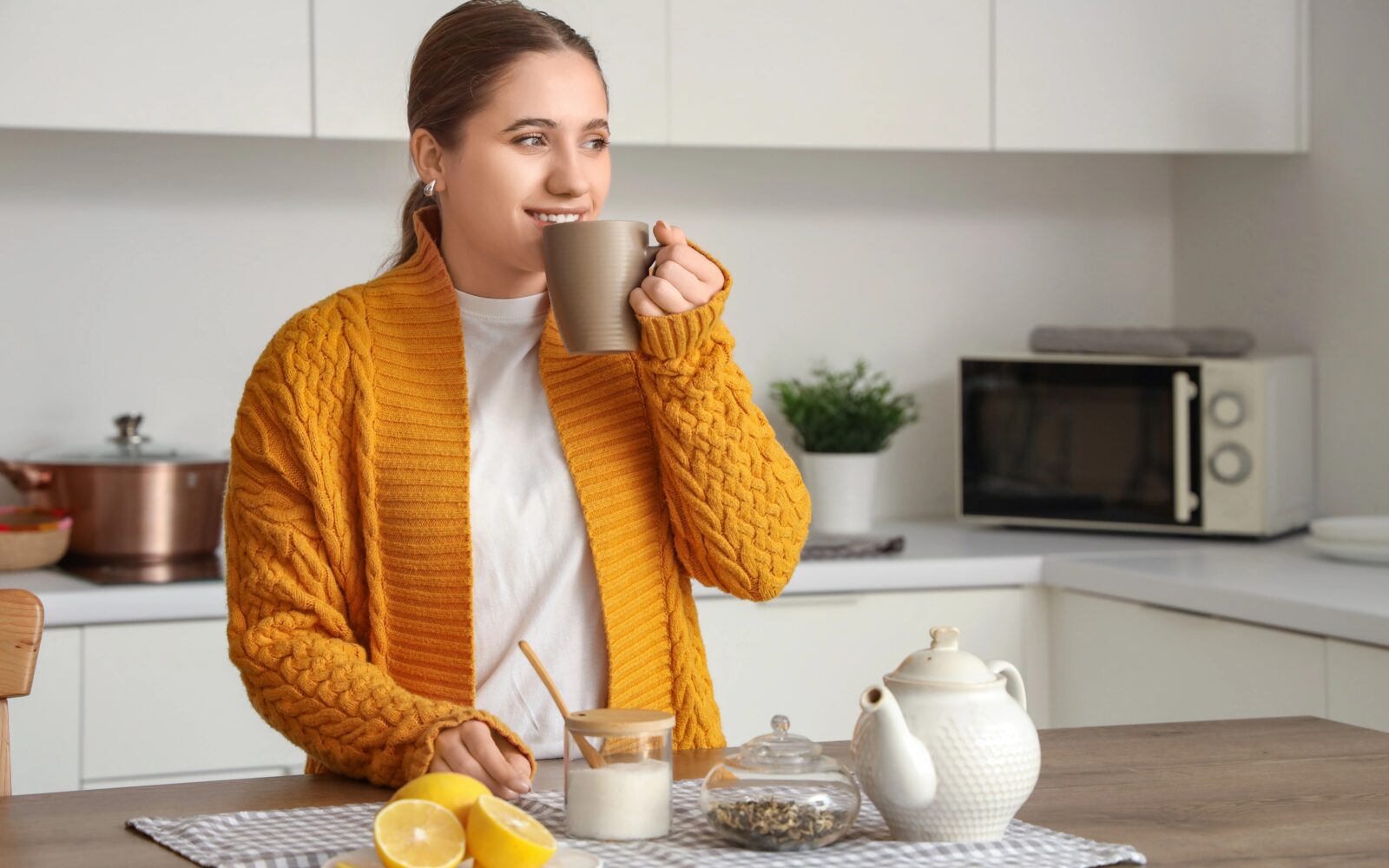 Ženska v kuhinji pije čaj z limono.