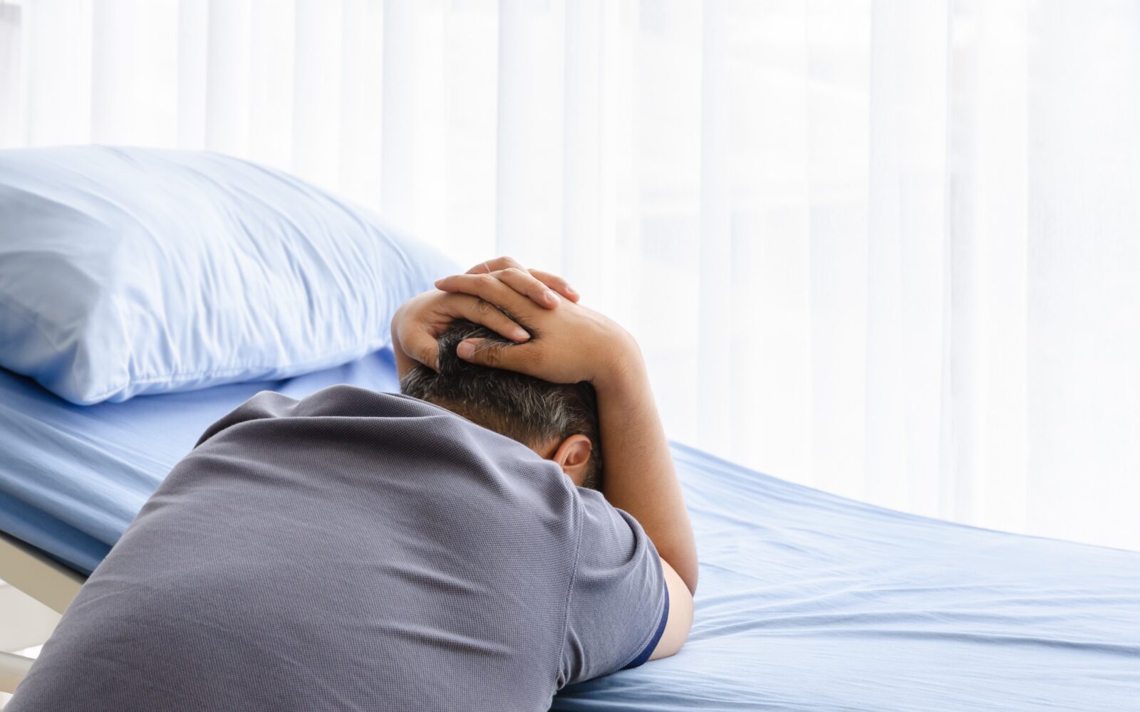 Starejši moški je naslonjen na prazno bolniško posteljo, žaluje