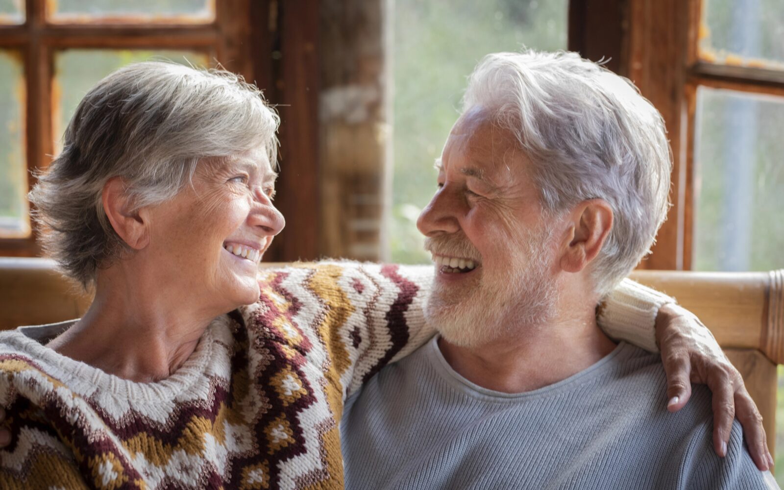 Starejša ženska in moški se objemata in smejita, sedita doma