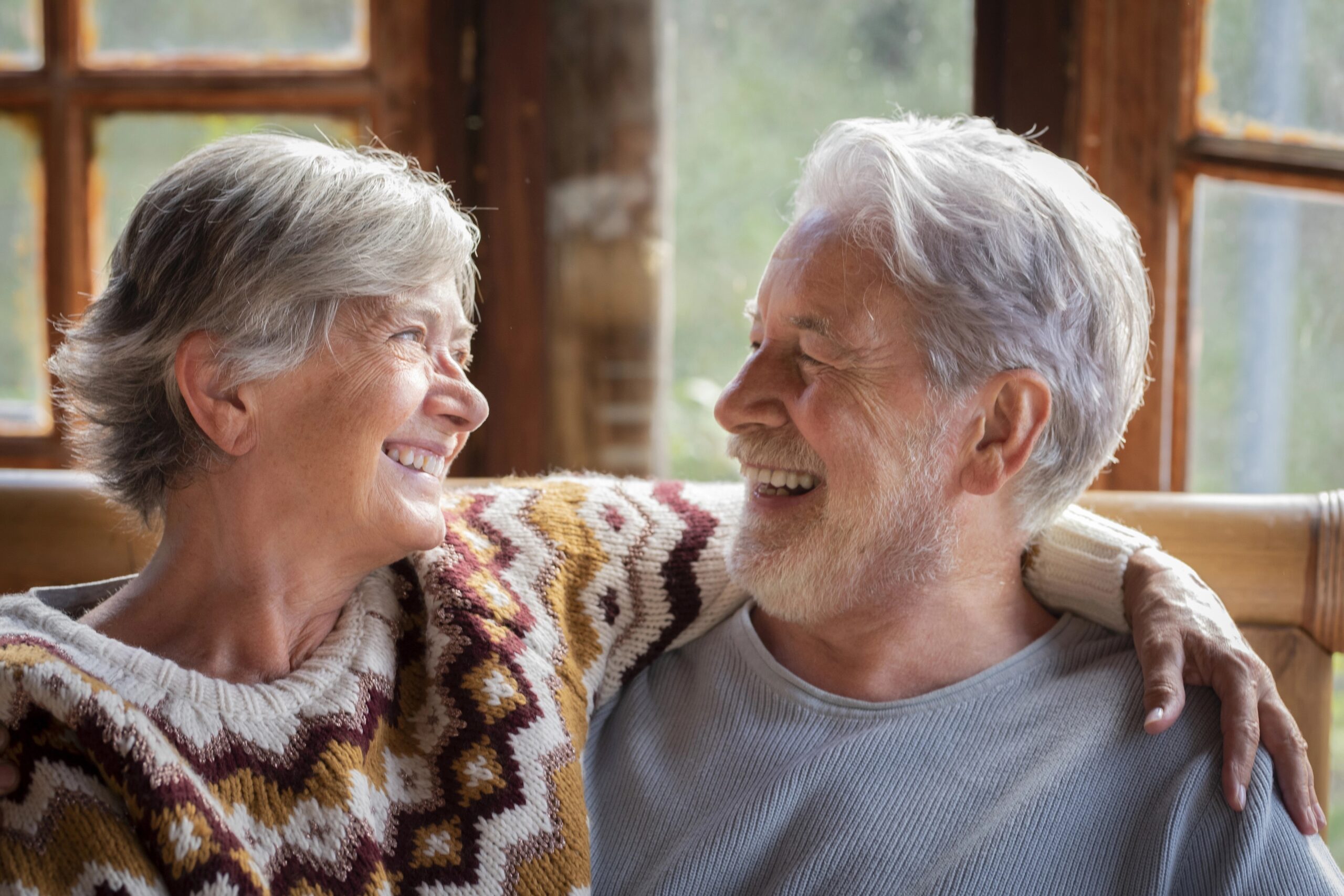 Starejša ženska in moški se objemata in smejita, sedita doma