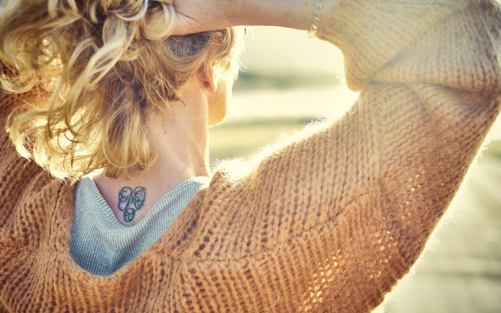 Ženska gleda sončni zahod, na hrbtu ima tetovažo