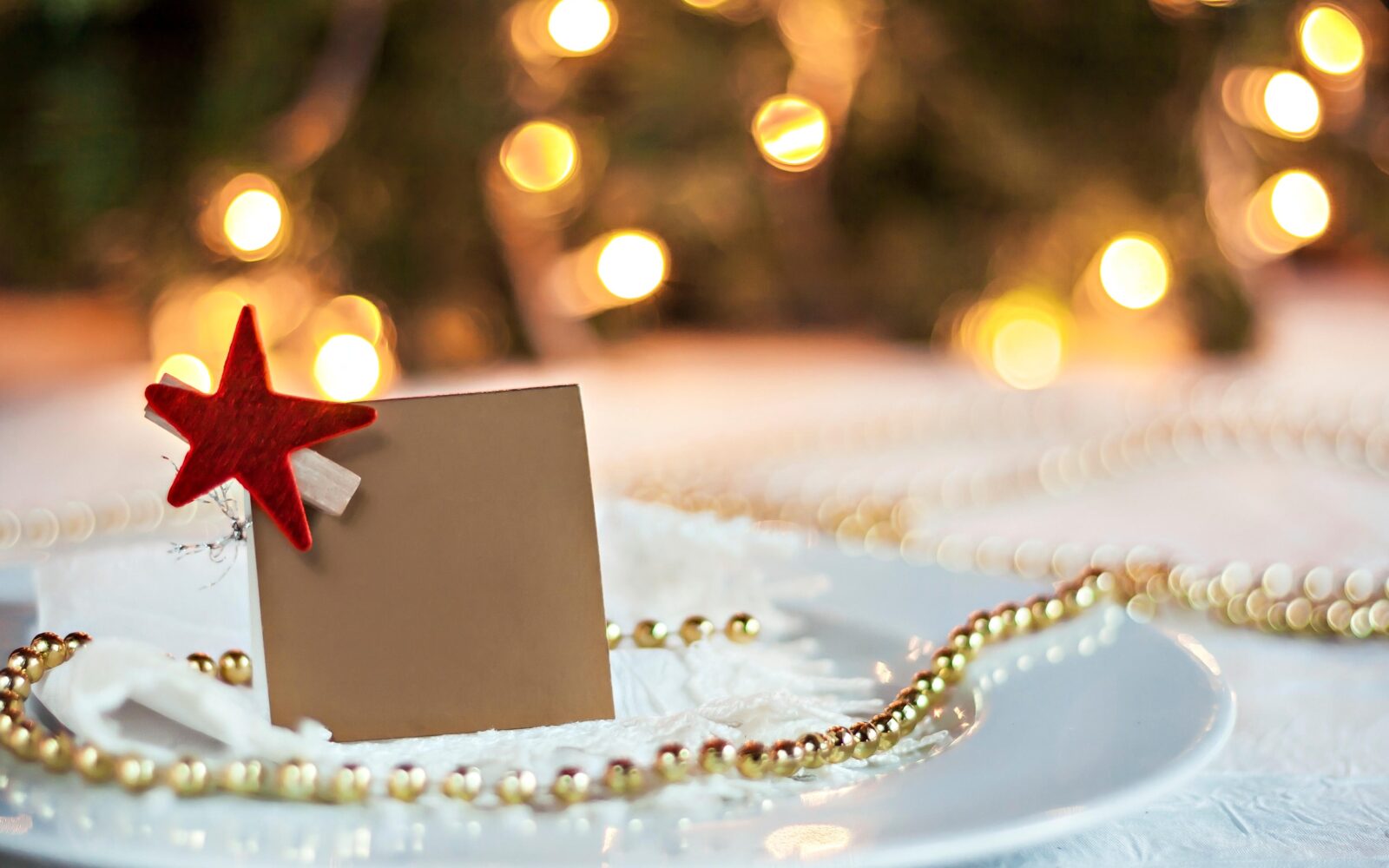 Praznična miza, okrašena s kartico z imenom gosta, rdečo božično zvezdo in zlatimi kroglicami