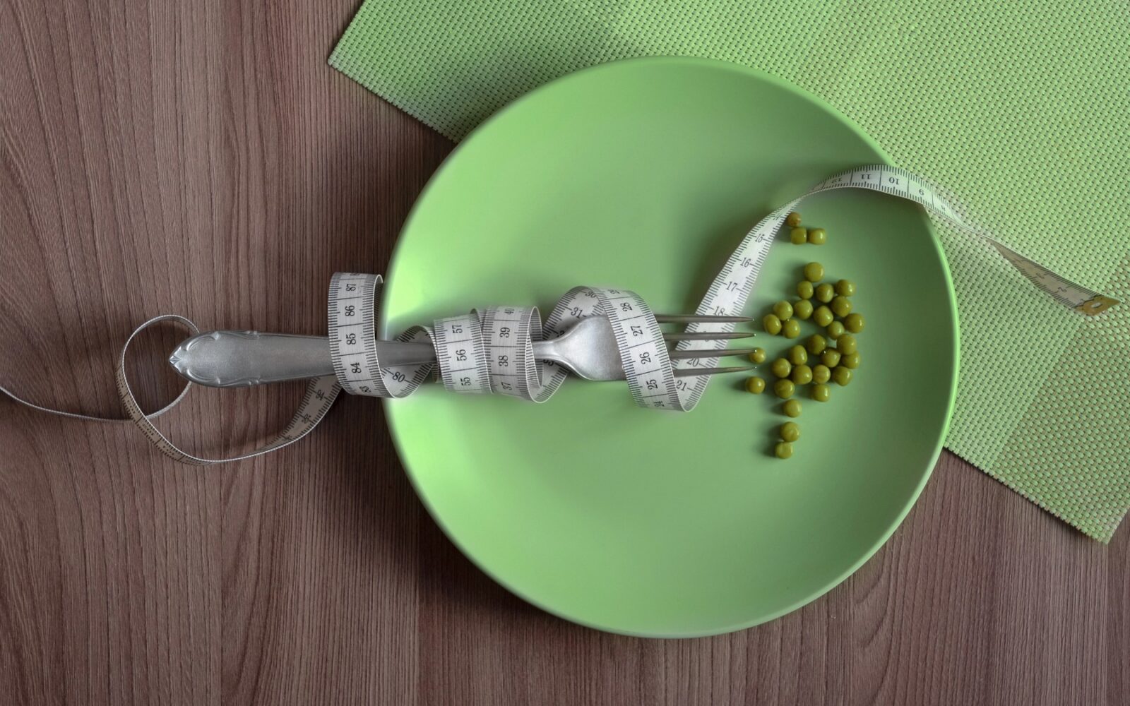 Stroga dieta: krožnik z malo hrane in merilni trak okoli pribora