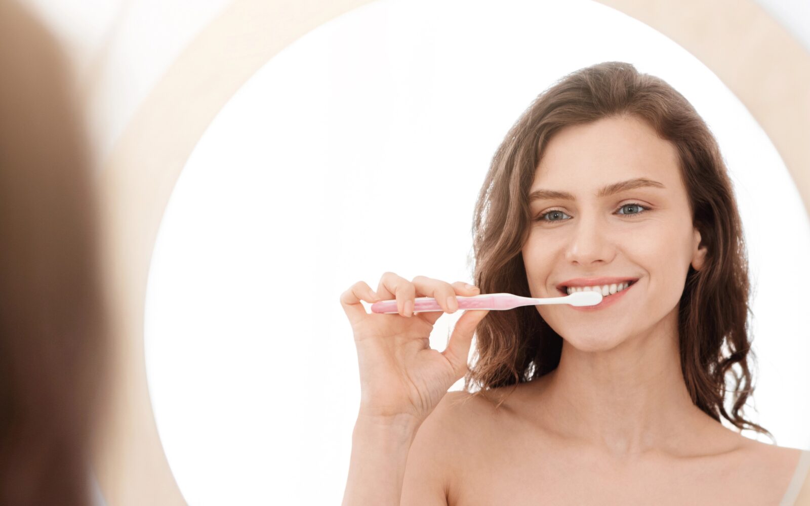 Mlada ženska si zadovoljno umiva zobe in se gleda v ogledalo - ustna higiena, temelj zdravega staranja