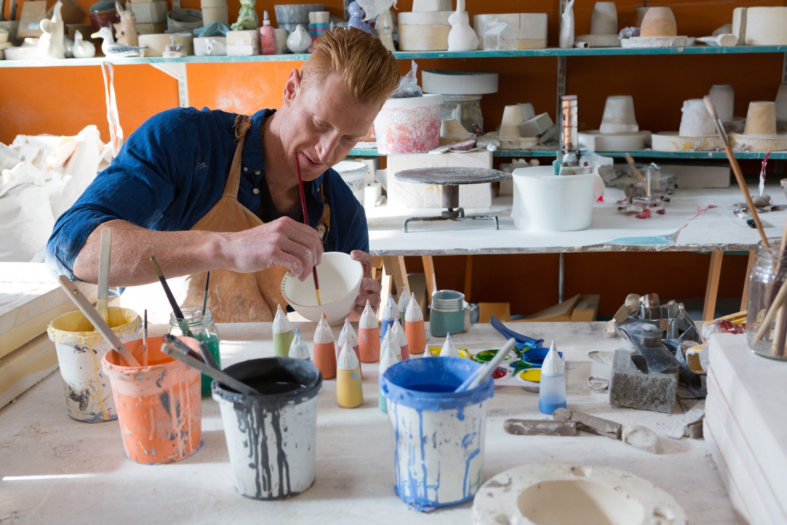 Mlad moški v slikarski delavnici meša barve in slika na skodelico - ustvarjalni počitek, ki ima številne koristi za naše telo in možgane.