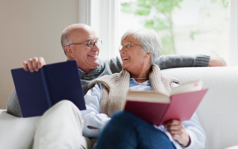 Nasmejan starejši par sedi na kavču in bere - zdravo staranje