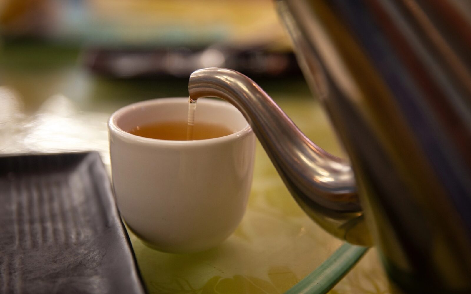 Natakanje čaja iz čajnika v belo skodelico