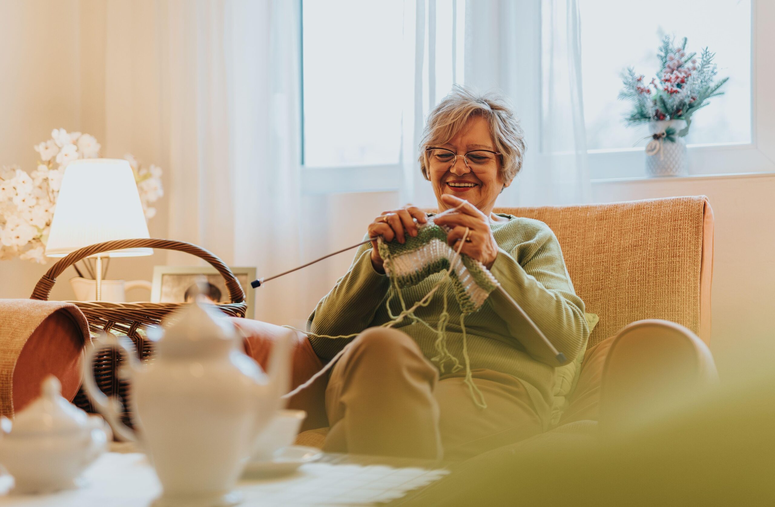 Starejša ženska zadovoljno sedi na naslanjaču in plete - aktivnost za spodbujanje čuječnosti