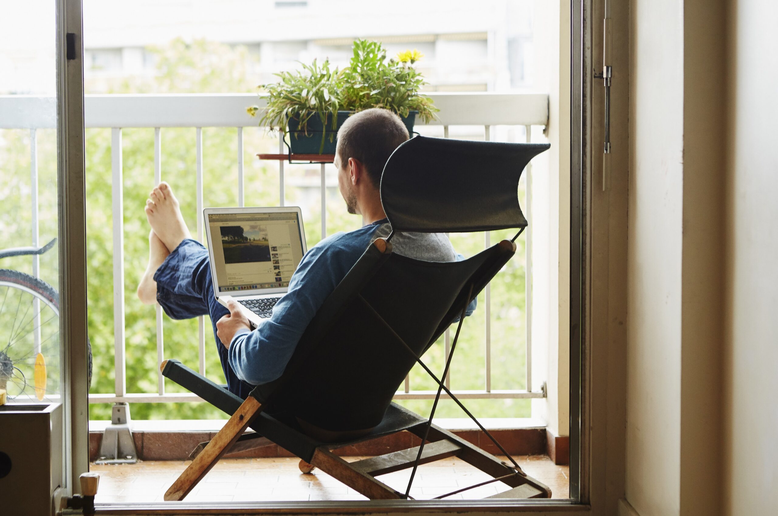 Moški ima v naročju računalnik in nekaj dela. Sedi na stolu