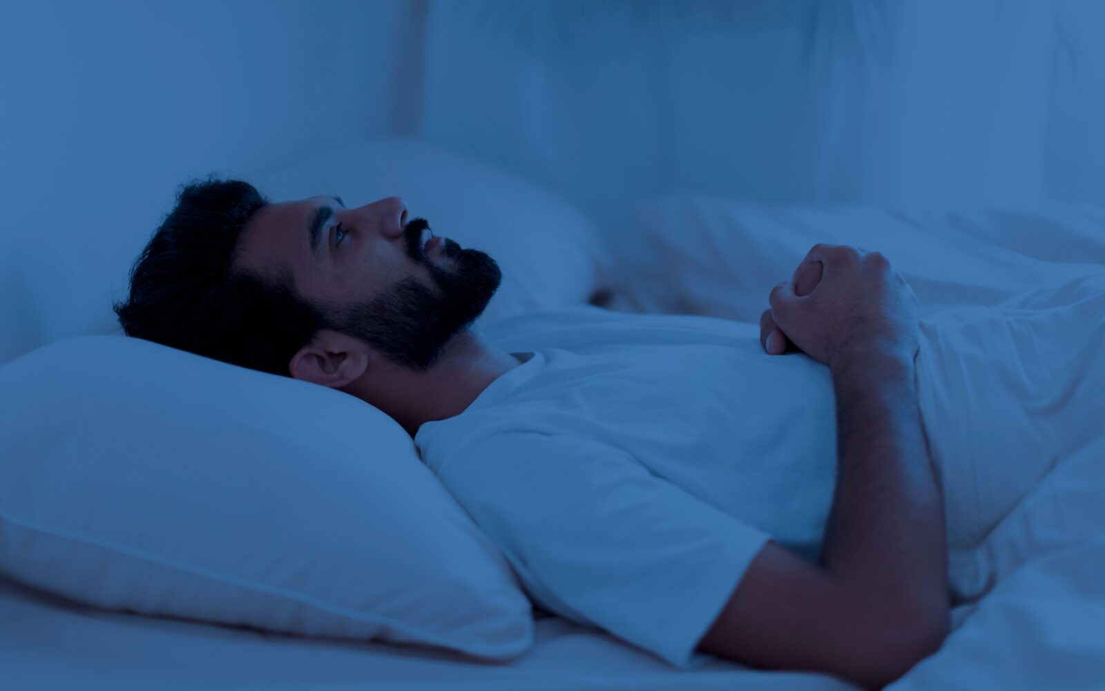 Moški leži ponoči v postelji in ne more spati, strmi v strop