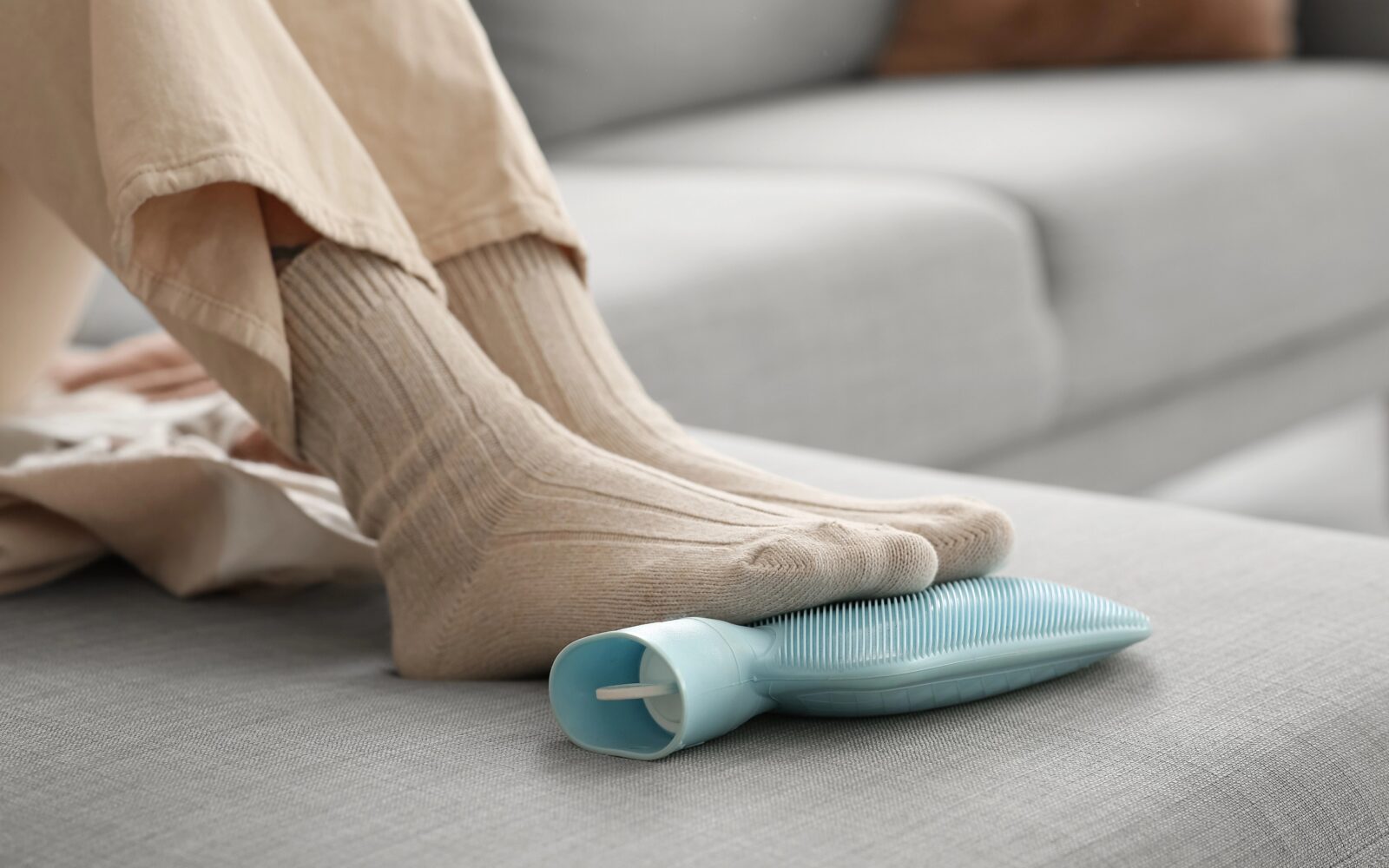 Ženska si na kavču doma greje noge z grelno blazino.