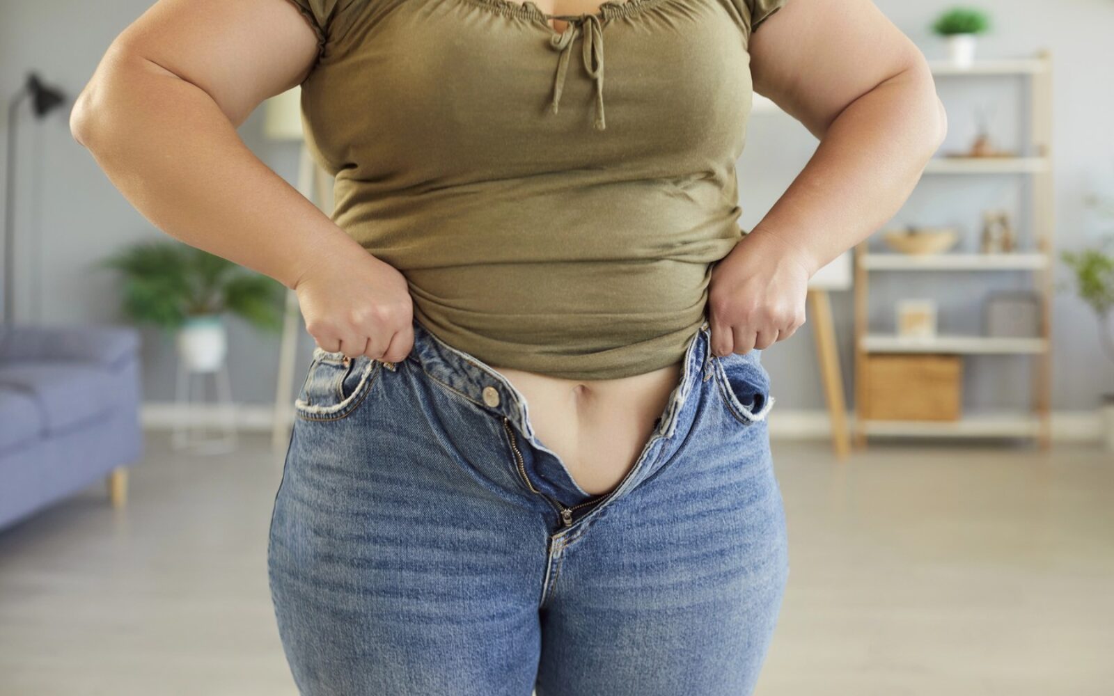 Ženska v menopavzi z težavami pri zapenjanju hlač zaradi trebušne maščobe - ponazoritev hormonskih sprememb po 40. letu