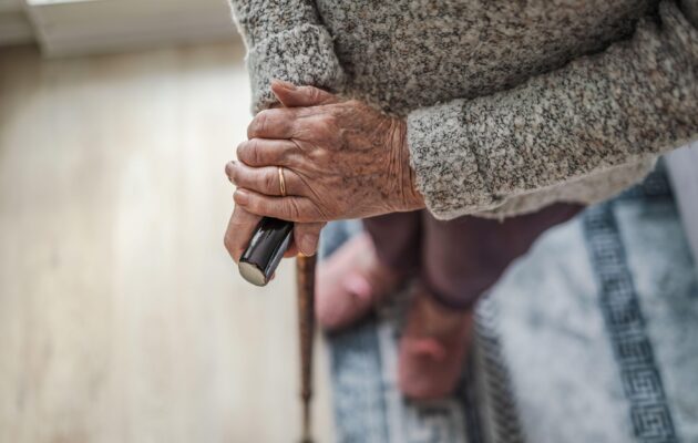 Starejša ženska stoji s sprehajalno palico v rokah