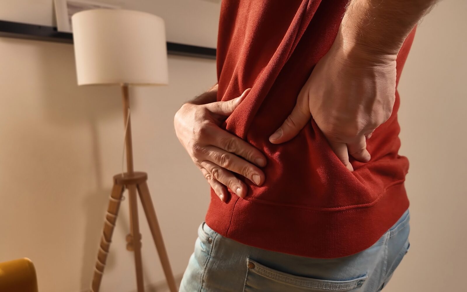 Moški v rdeči majici se drži za hrbet zaradi bolečine, misleč, da gre za nategnjeno mišico, a gre za hernijo diska