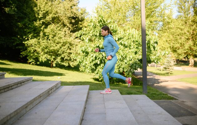 Mlada ženska med jutranjo telovadbo teče po stopnicah v parku