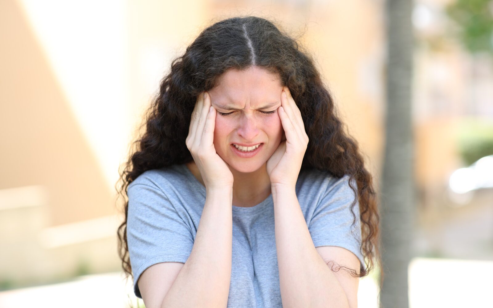 Mlada ženska se na cesti drži za glavo zaradi nepričakovanega glavobola, ki je simptom migrene