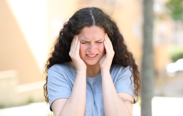 Mlada ženska se na cesti drži za glavo zaradi nepričakovanega glavobola, ki je simptom migrene