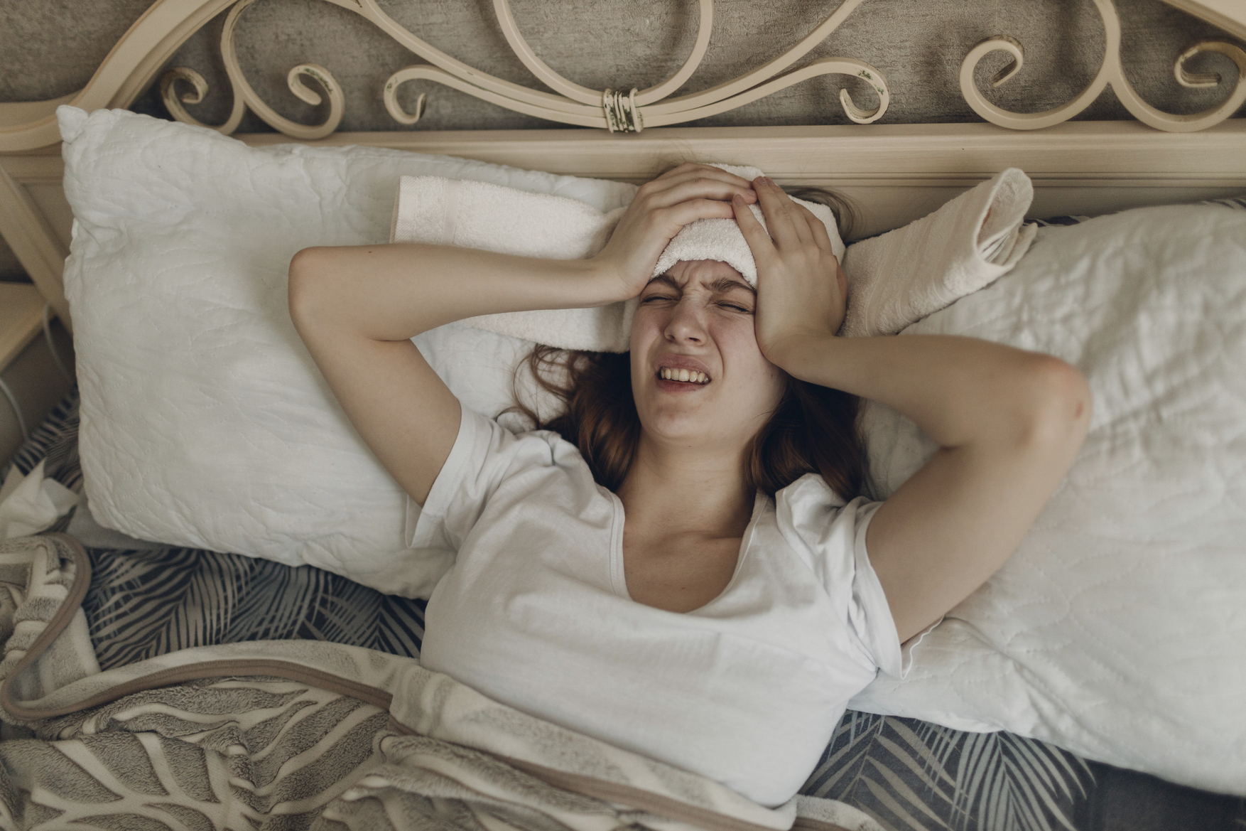 Ženska leži v postelji in ima na glavi obkladek - migrena