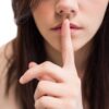 Ženska drži prst na ustnicah, simbolika skrivnosti