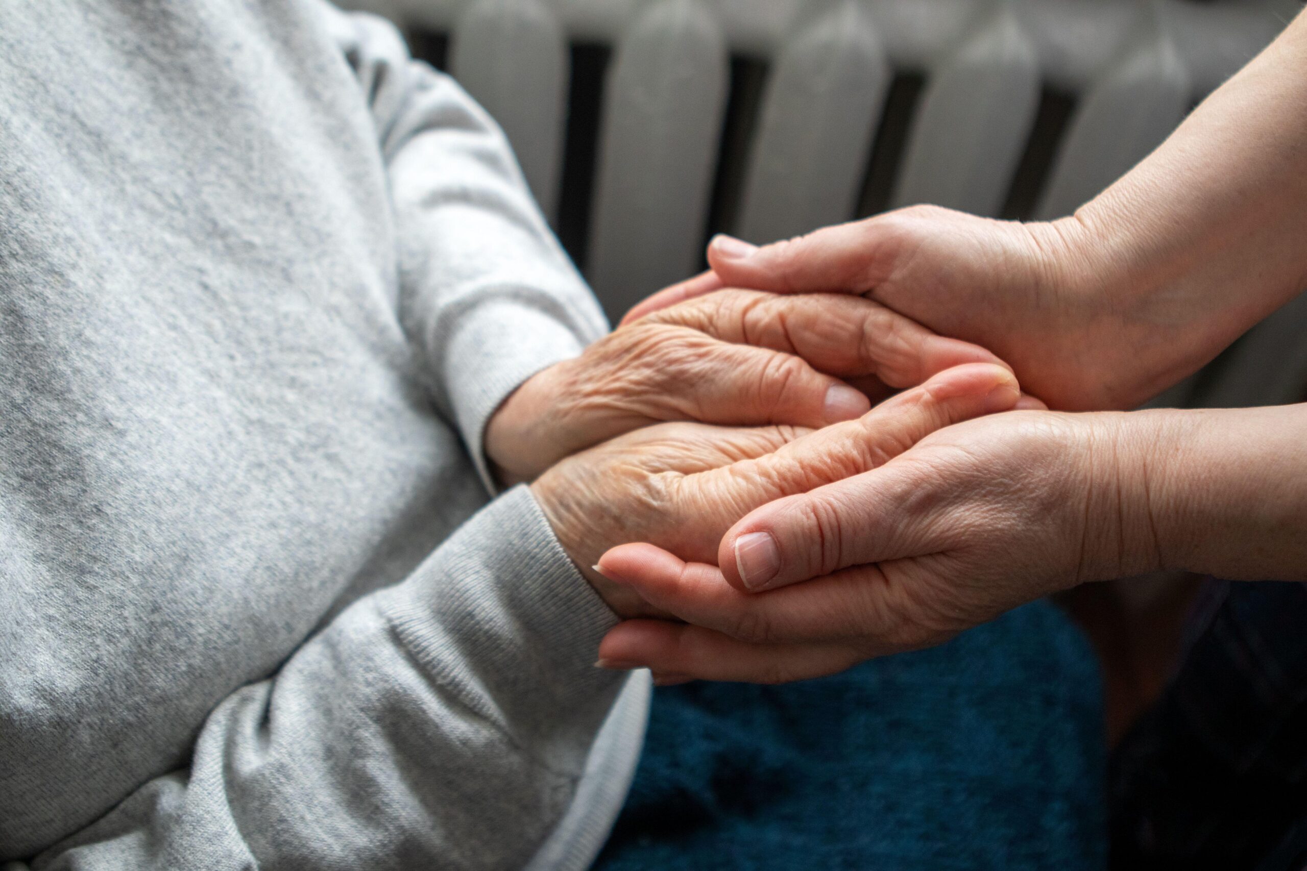 mlajša negovalka v rokah drži dlani starejše osebe; znak sočutja in