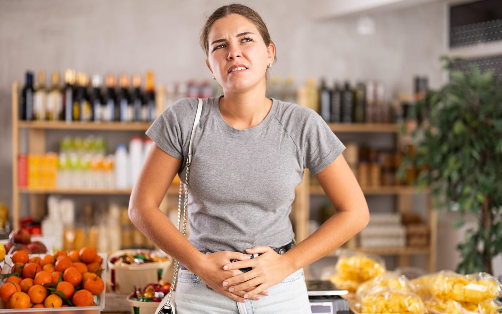 Ženska občuti potrebo po odvajanju blata med nakupovanjem, zato se drži za trebuh.