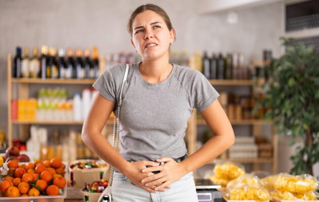 Ženska občuti potrebo po odvajanju blata med nakupovanjem, zato se drži za trebuh.
