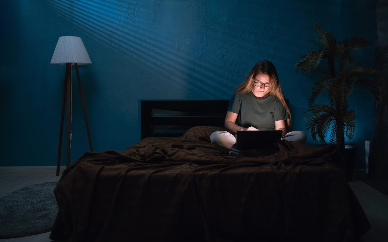 Ženska v temi ponoči sedi na postelji in dela za računalnikom - nočni tip osebe