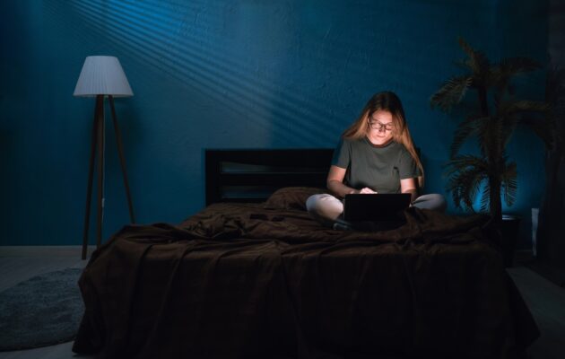 Ženska v temi ponoči sedi na postelji in dela za računalnikom - nočni tip osebe