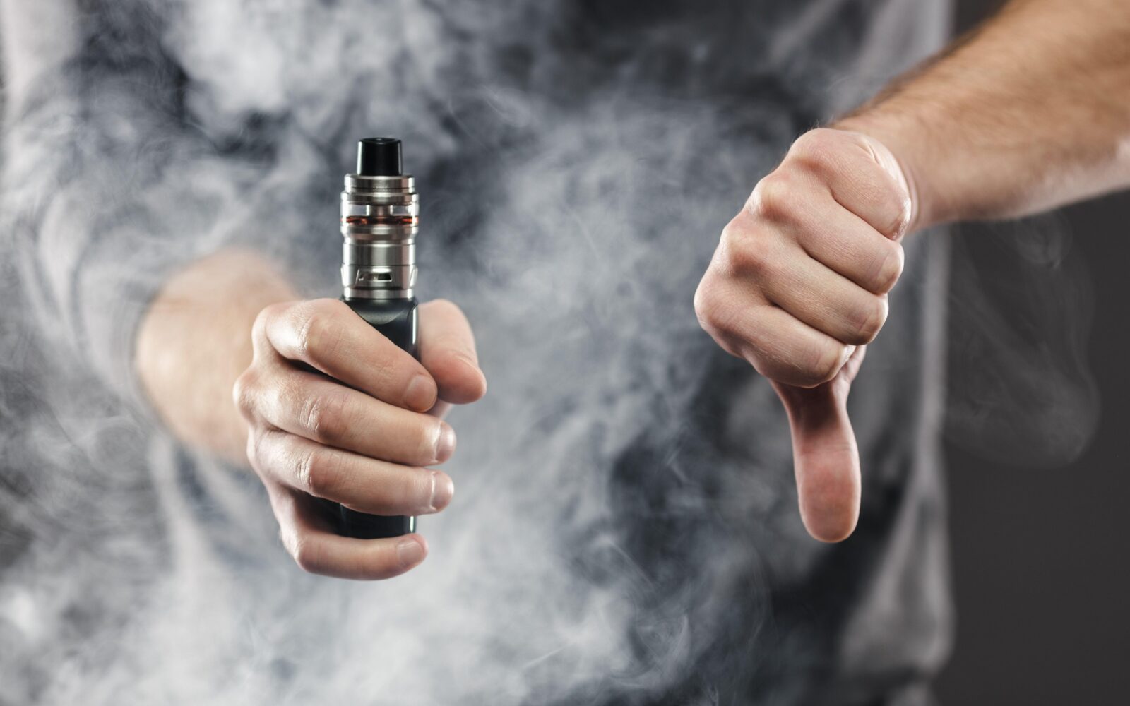 Moški v eni roki drži elektronsko cigareto (e-cigareto, vejp), z drugo pa simbolično kaže, da to odklonilen znak - prst obrnjen navzdol