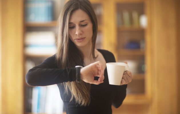 Lepa ženska v eni roki drži skodelico in gleda na uro