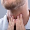 Moški si drži vrat kot prikaz možnih simptomov raka ustnega žrela, povezanega s HPV