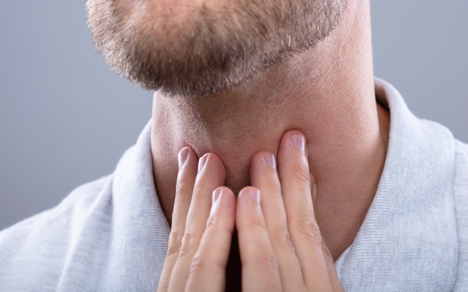 Moški si drži vrat kot prikaz možnih simptomov raka ustnega žrela, povezanega s HPV