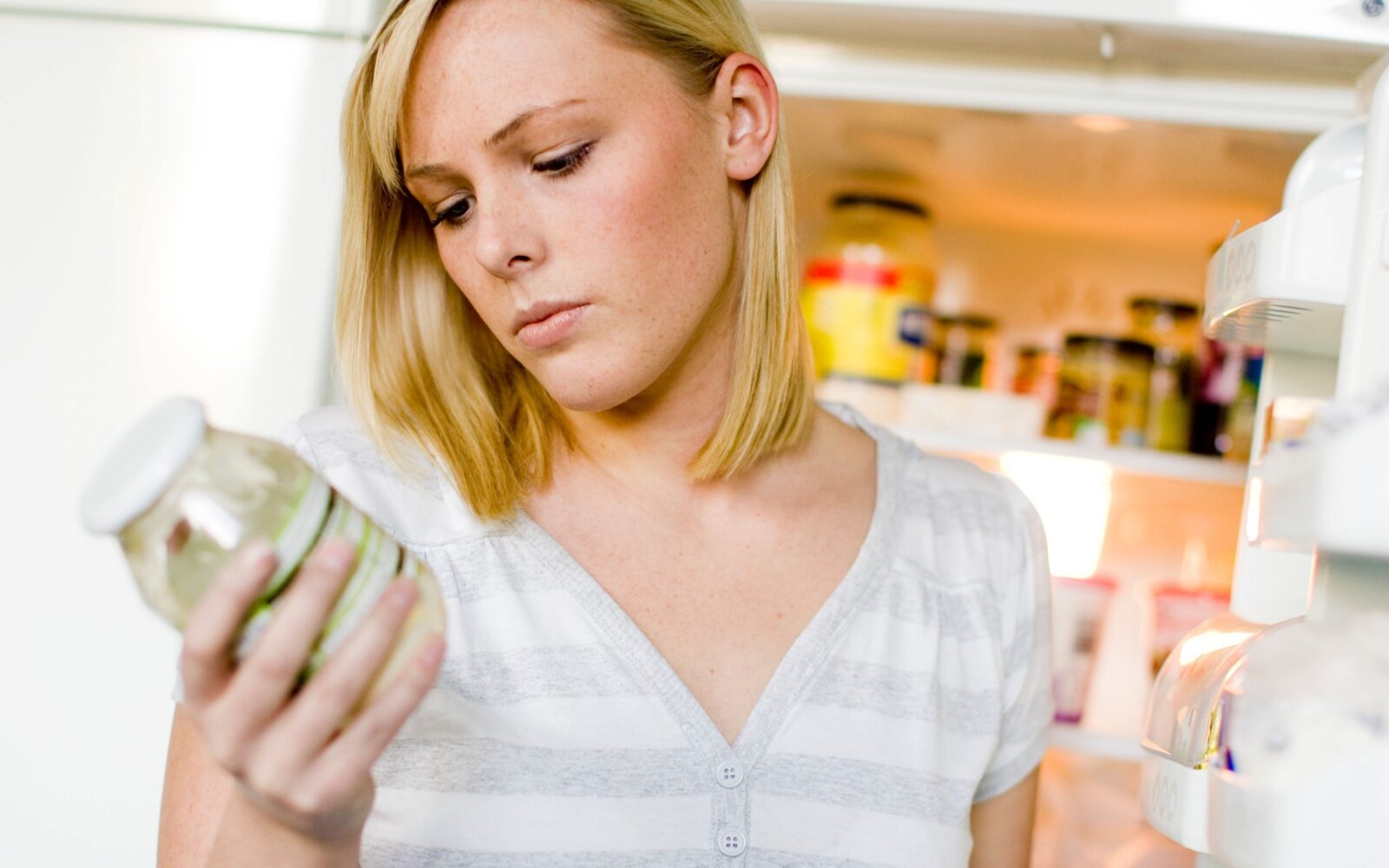 Ženska pred hladilnikom gleda na embalaži steklenega kozarca rok uporabe