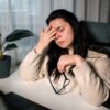 Ženska si v pisarni utrujeno mane oči in se drži za glavo - izgorelost pri ženskah