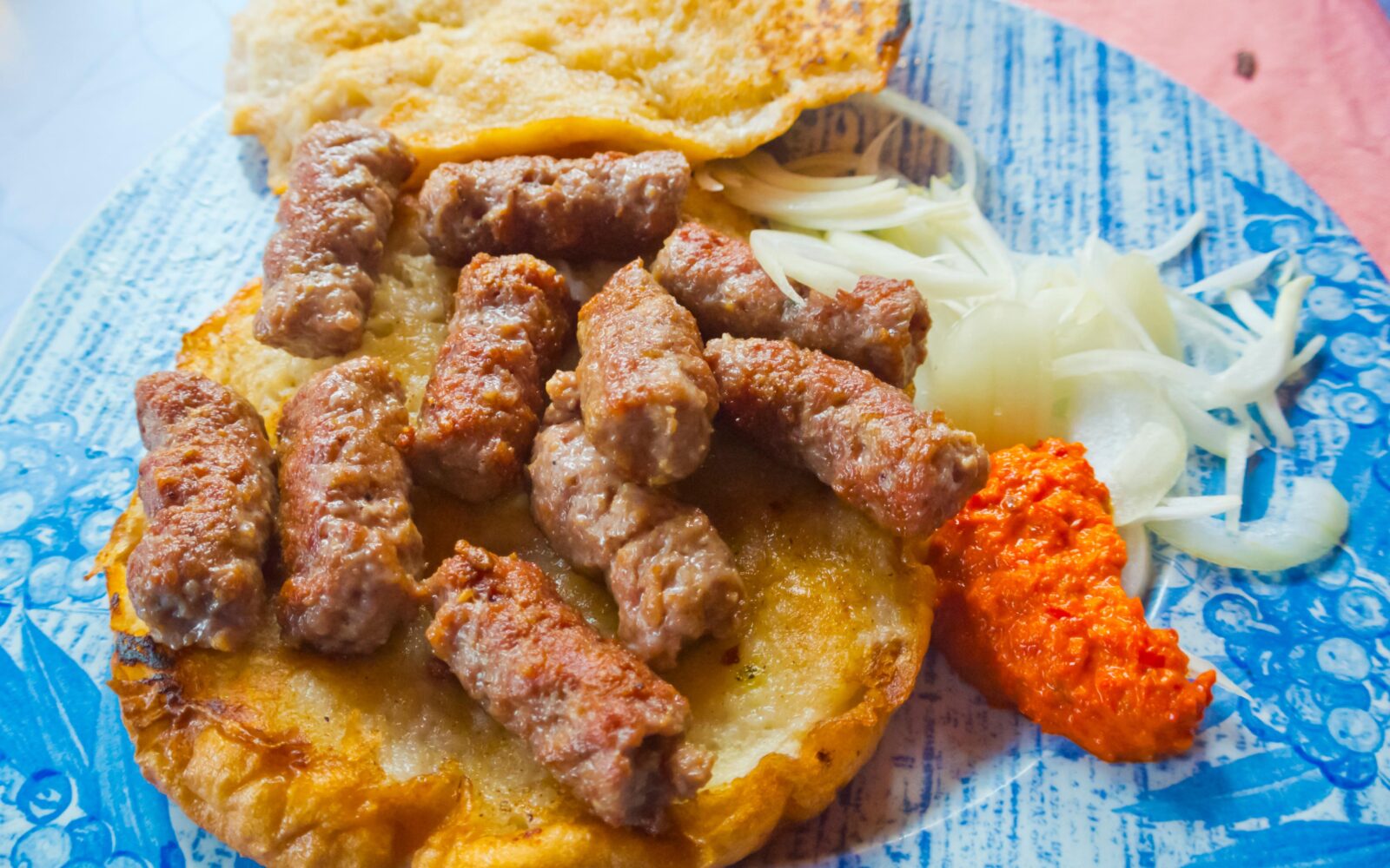 Porcija čevapčičev na somunju z ajvarjem in čebulo na krožniku