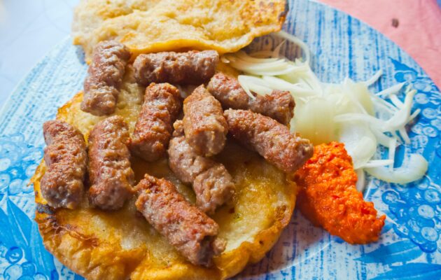 Porcija čevapčičev na somunju z ajvarjem in čebulo na krožniku